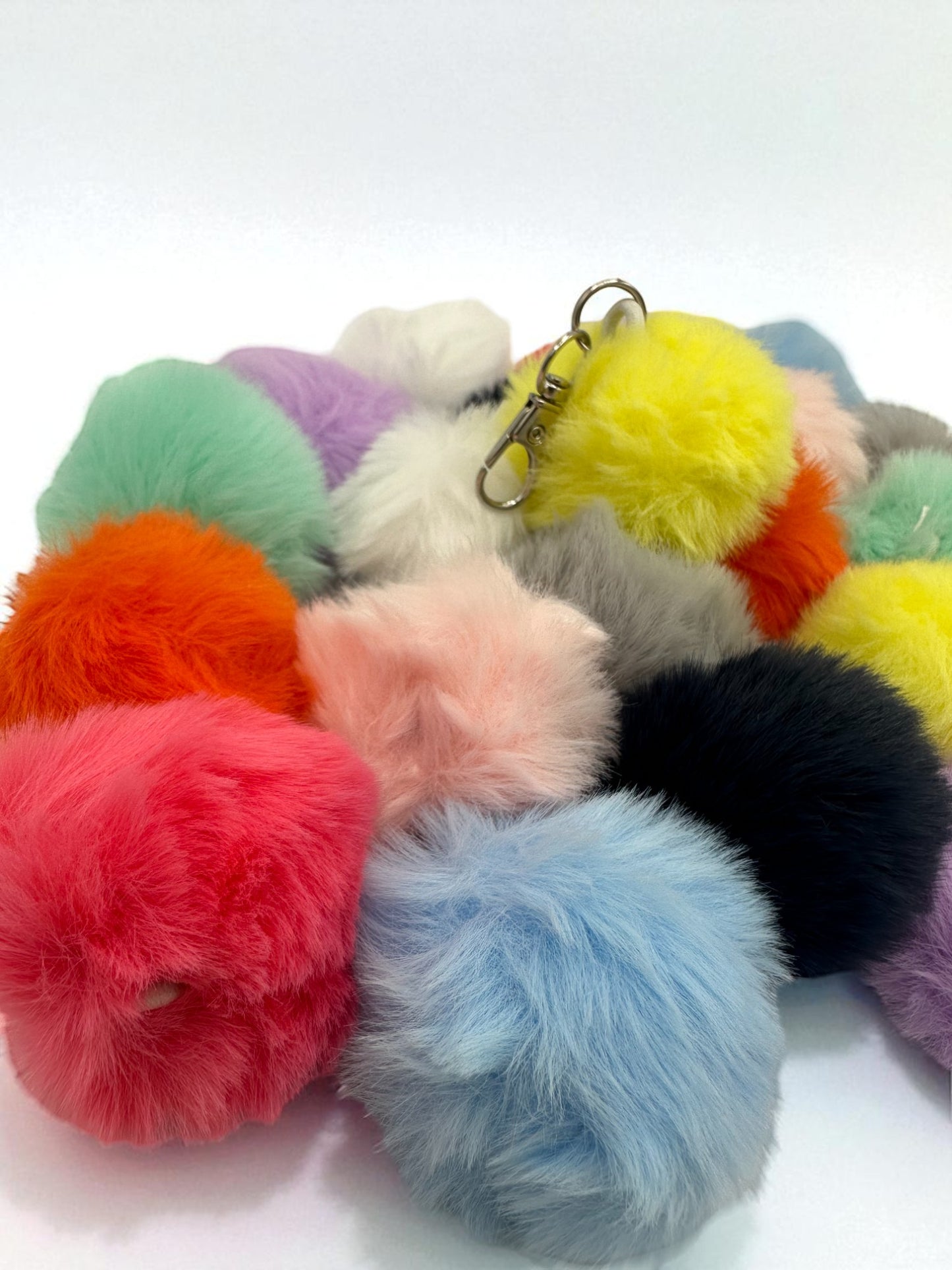 Assortment of fluffy sensory plush balls in various bright colors including pink, blue, yellow, orange, and purple, each with a keychain clip.