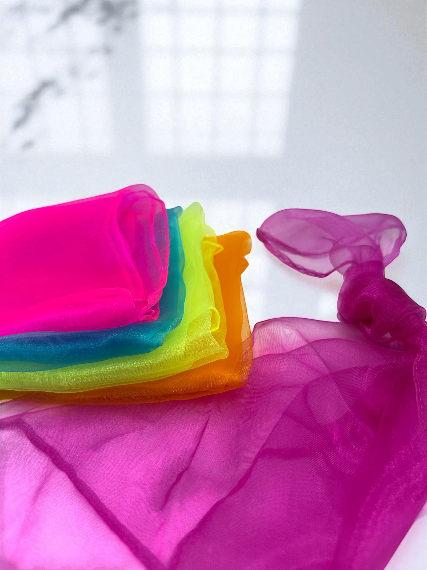 Sensitive Little Souls vibrant organza sensory scarf in neon pink, teal, lime green, and orange, with a fuchsia scarf draped.