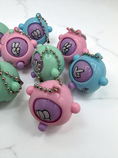 Sensitive Little Souls pastel pink, blue, and green plastic rock-paper-scissors game sensory toy with keychain. Features a purple face with hand gestures.